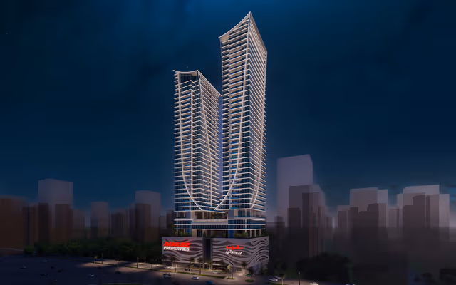 Elitz by Danube – twin curved-glass towers at night above the Danube podium in JVC